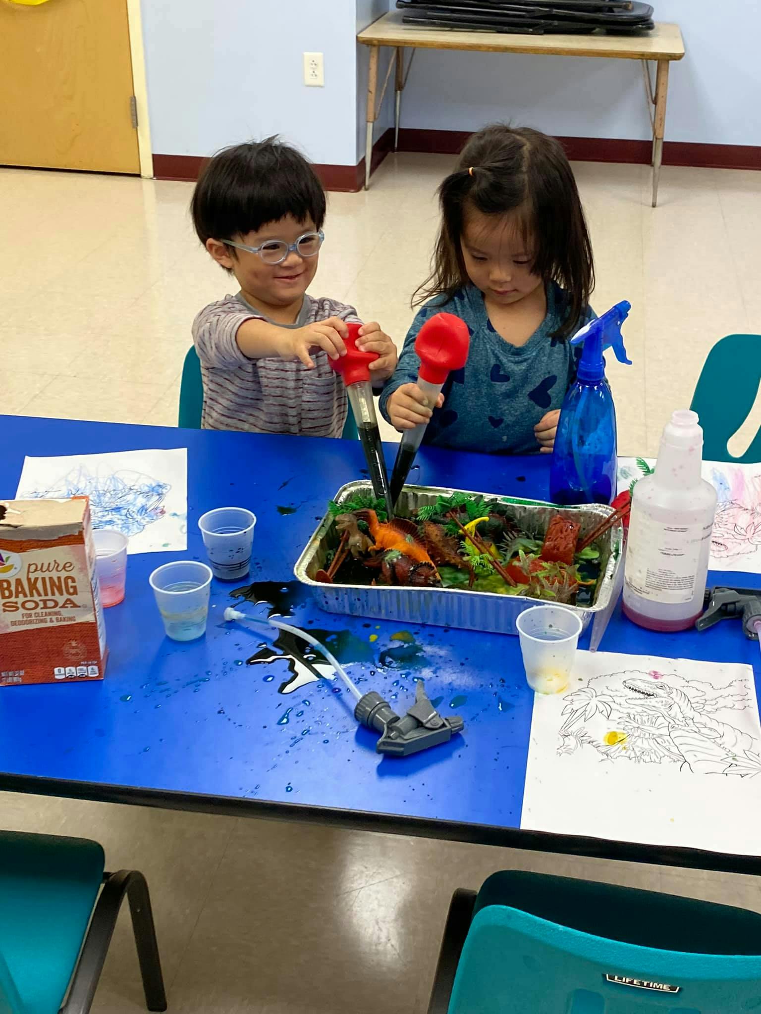 Two children playing with a science experiment on a blue table