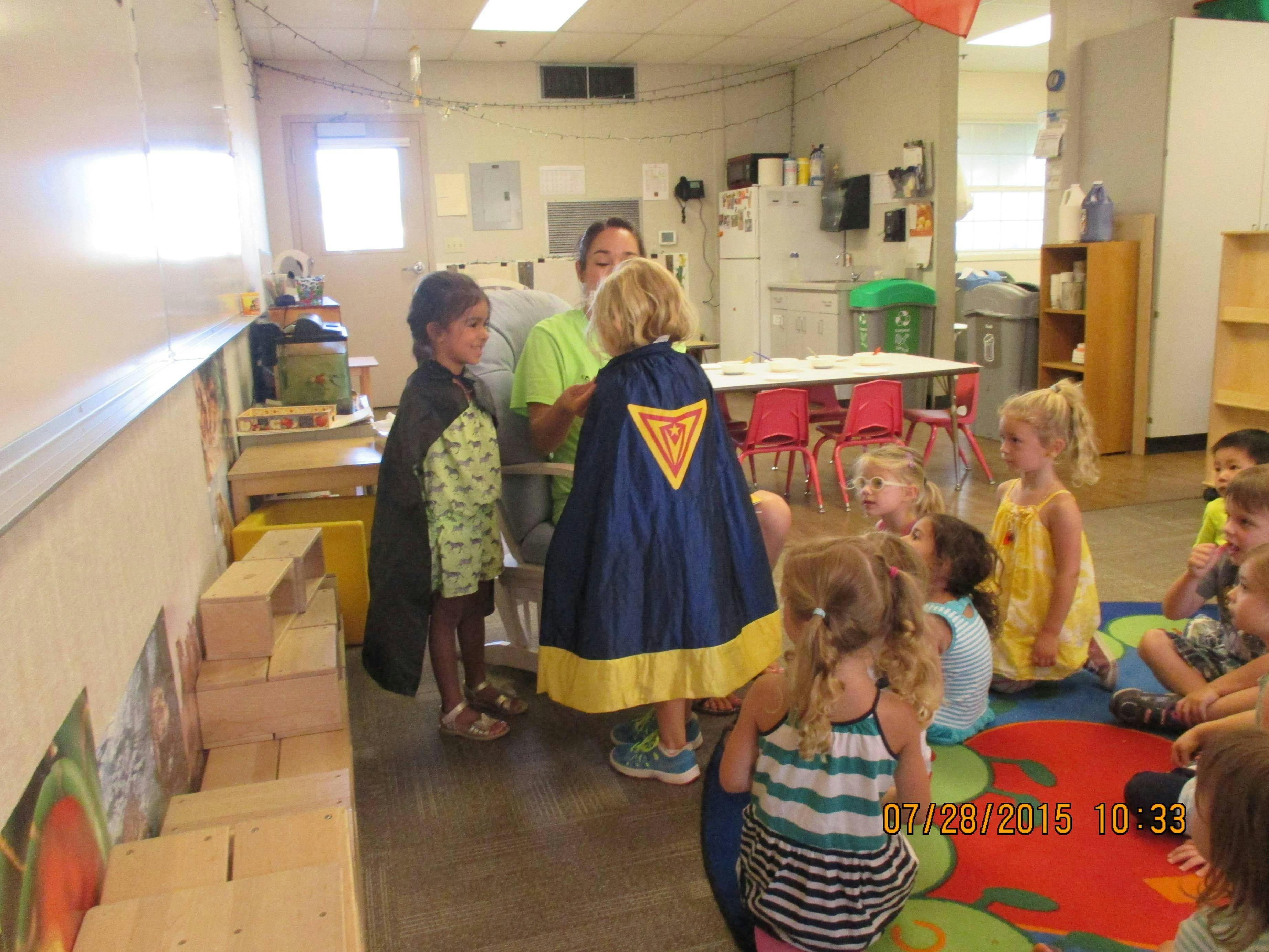 Adult and children in a classroom, two children wearing capes