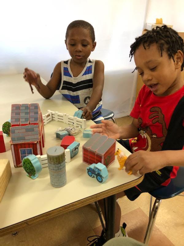 Two children playing with toy farm buildings and vehicles on a table