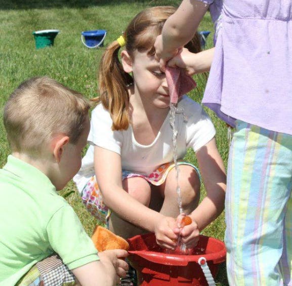 Children playing with water and sponges in a red bucket outdoors