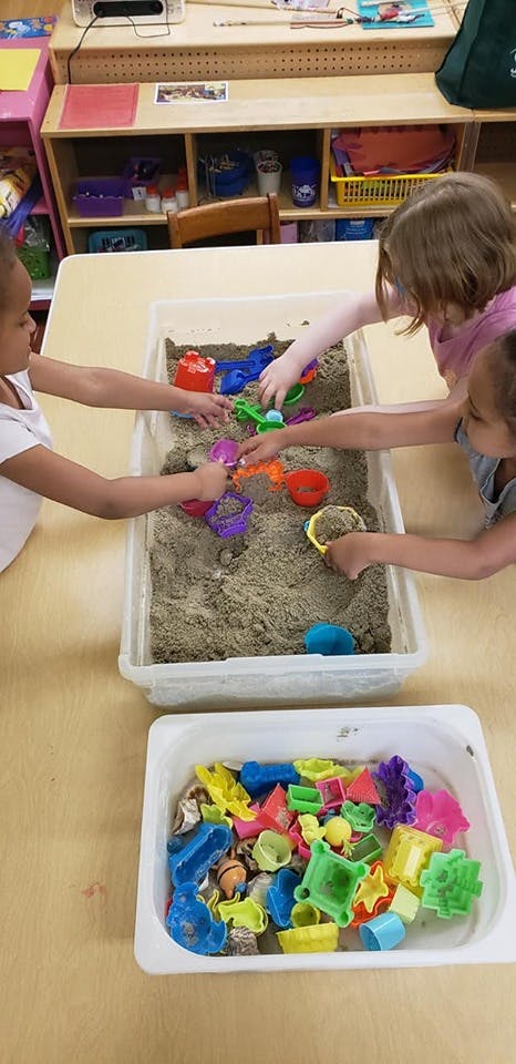 Three children playing in a sand table with colorful sand toys