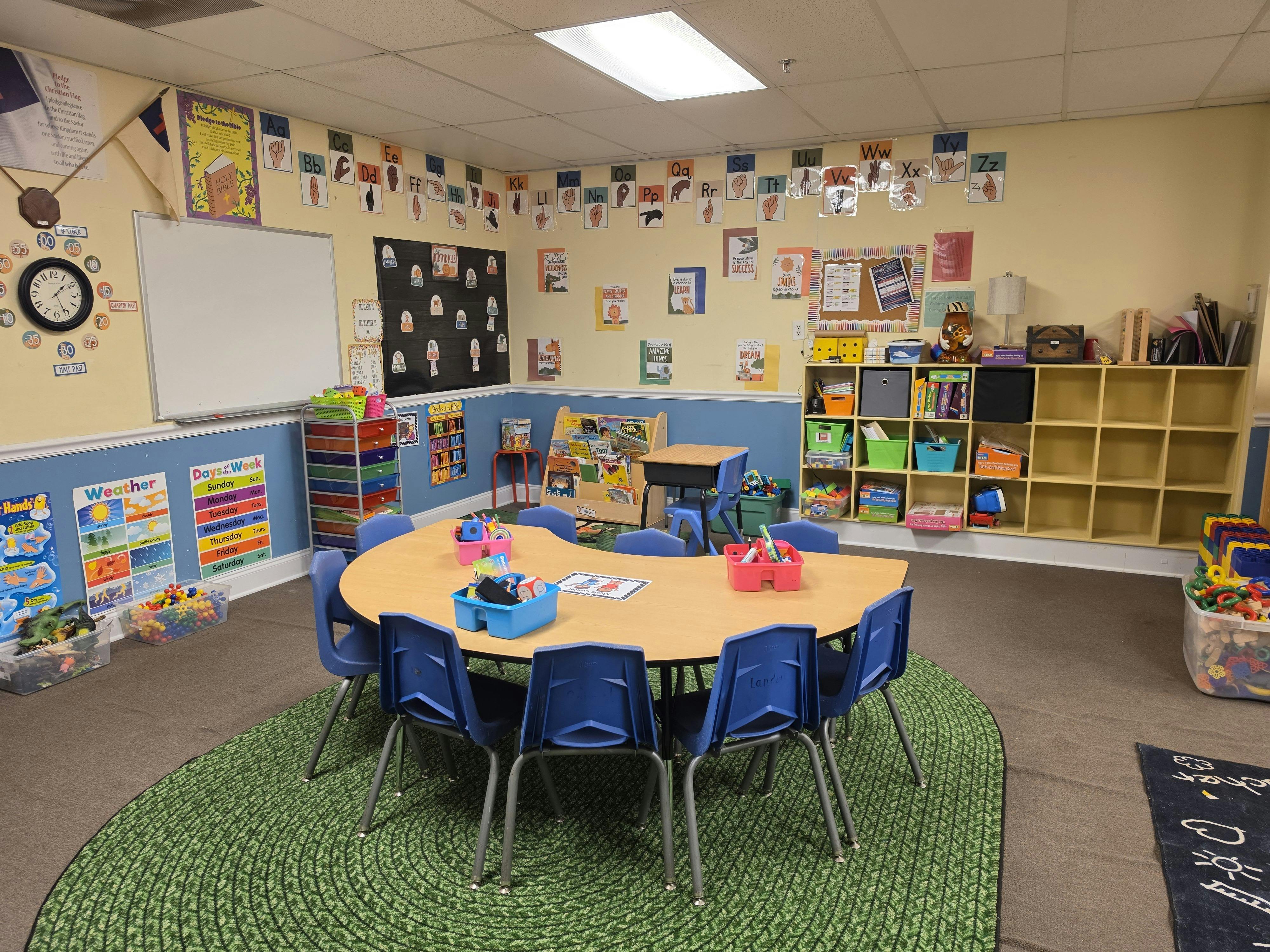 A colorful classroom with a round table and blue chairs, educational posters on the walls