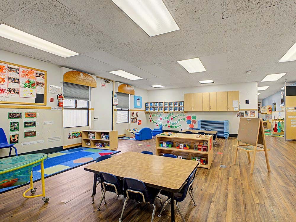 Empty classroom with small tables and chairs, shelves, and art on the walls