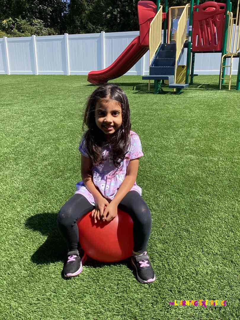 Child sitting on a red bouncy ball on artificial grass