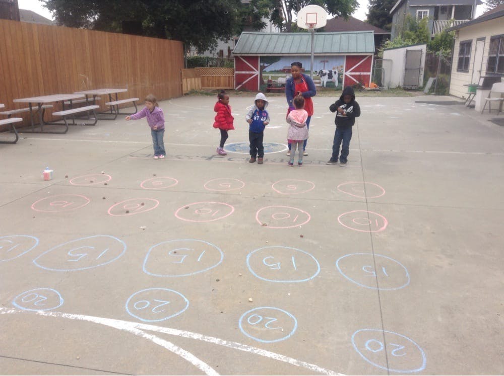 Children and an adult standing on a paved area with chalk drawings