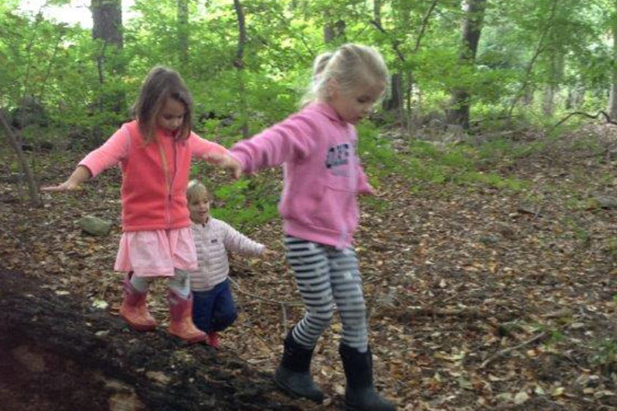 Two children and a baby balancing on a fallen log in a forest