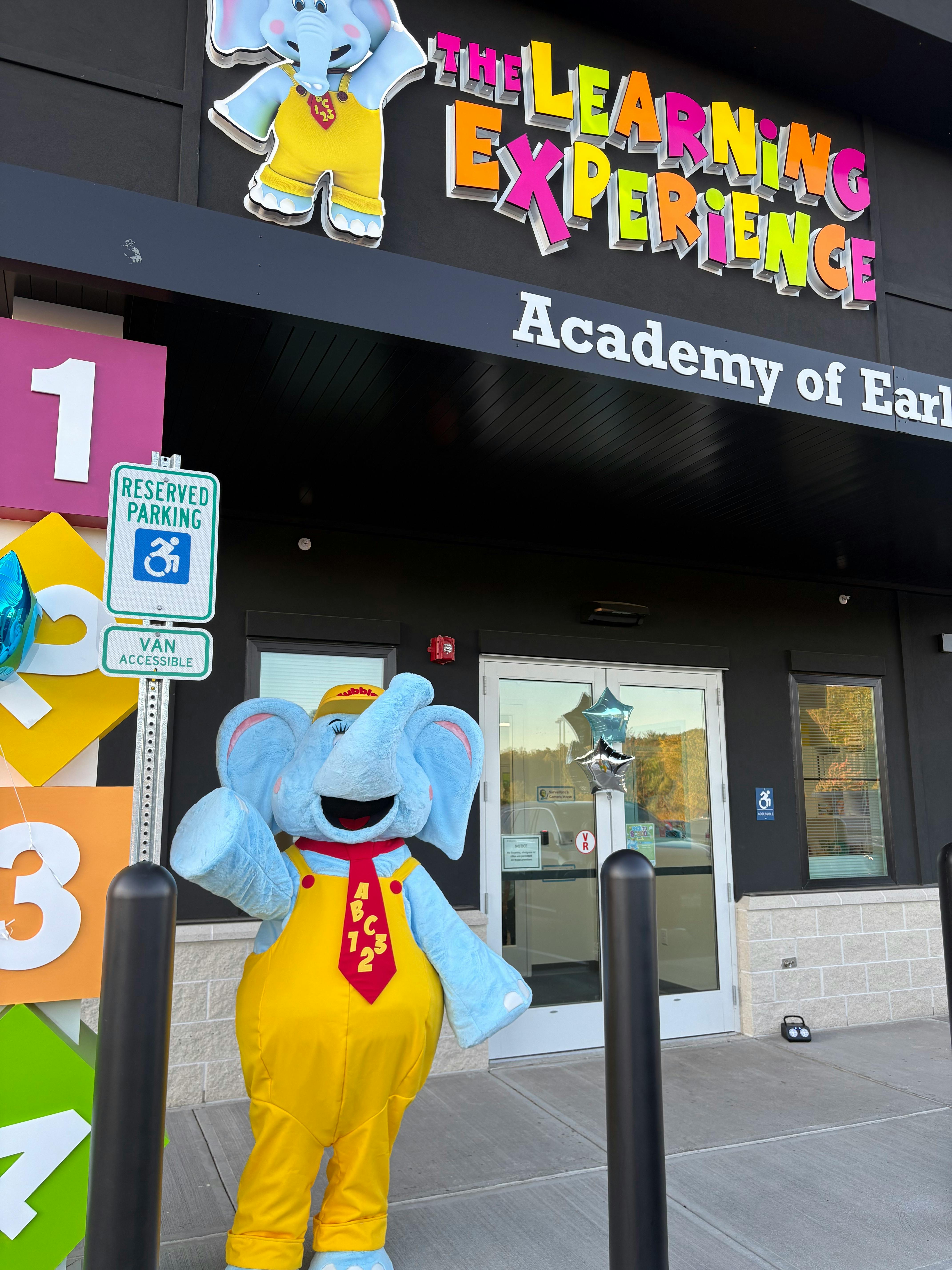 Elephant mascot outside a building with "The Learning Experience" signage