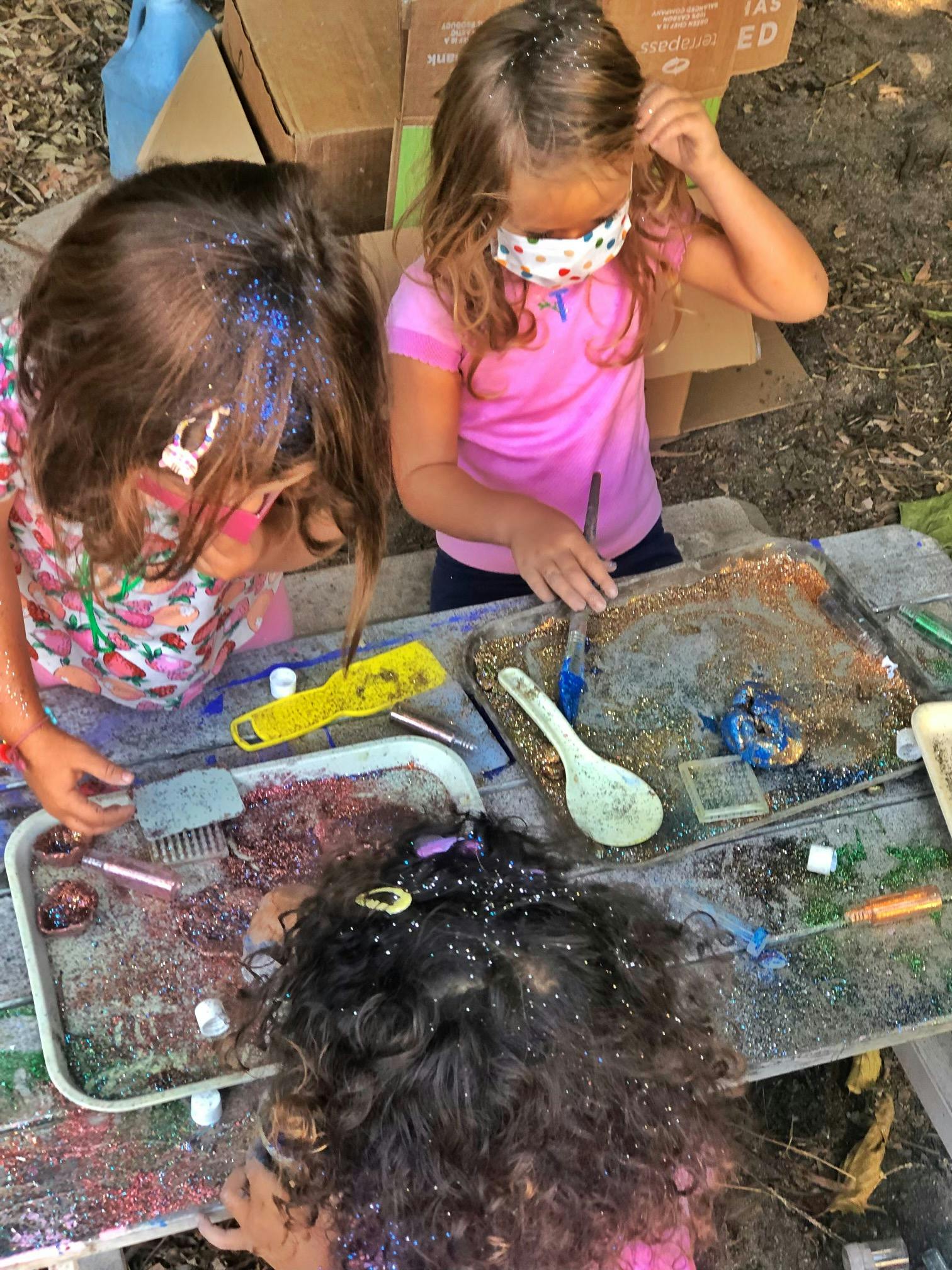 Three children playing with glitter and other craft materials on a table