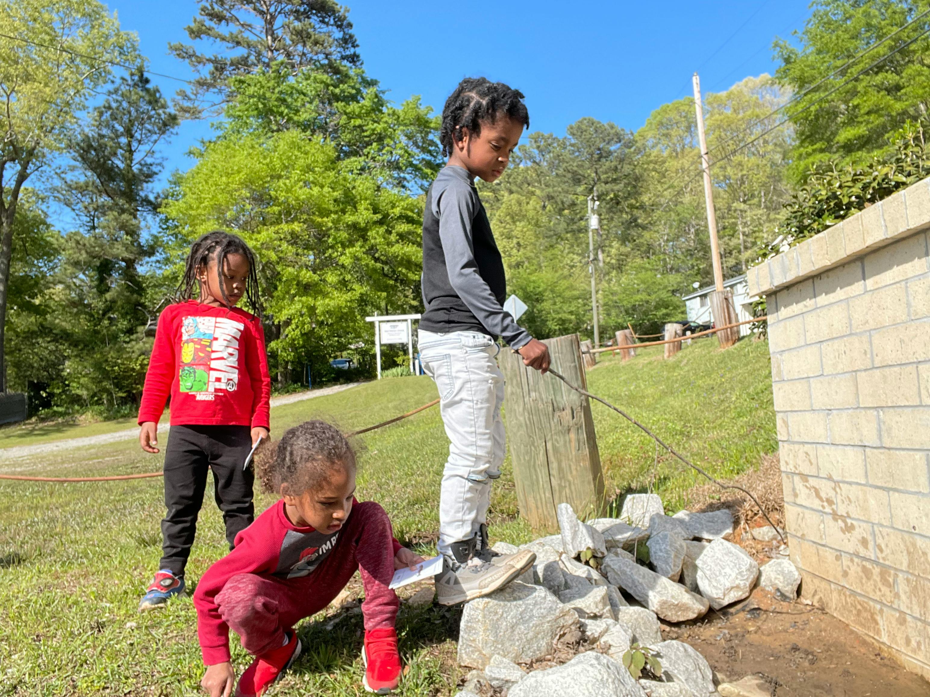 Three children playing outdoors near a stone wall