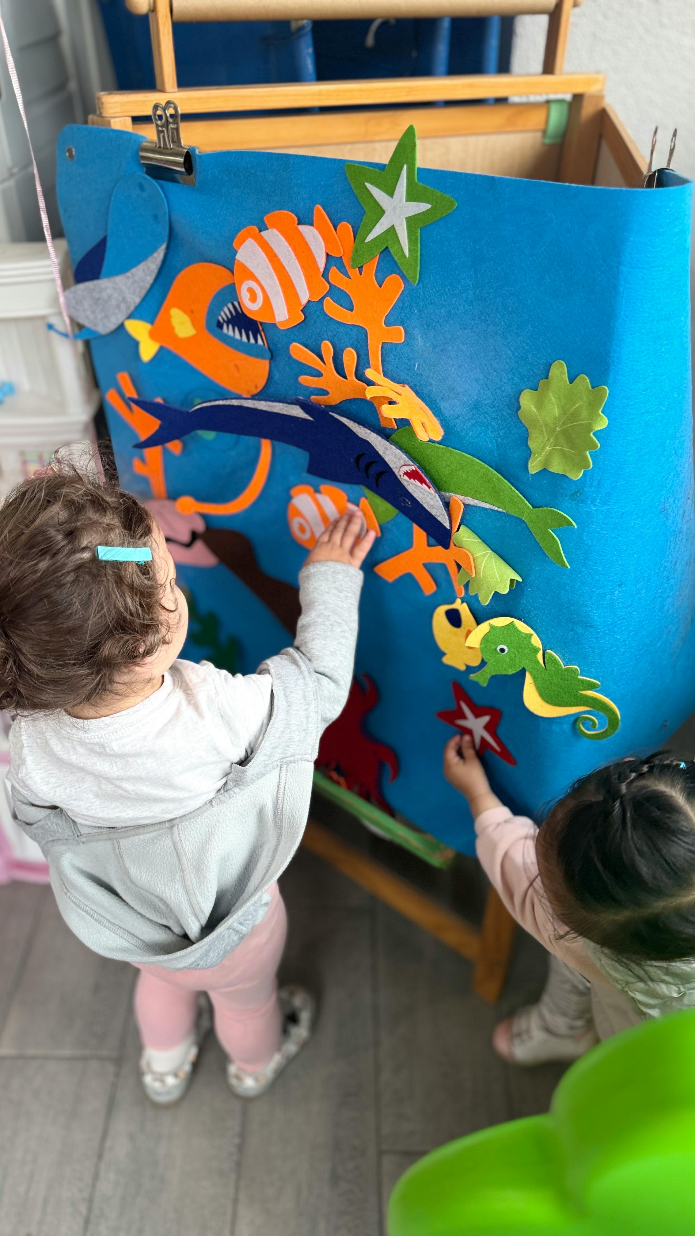 Two children playing with felt sea creatures on a blue board