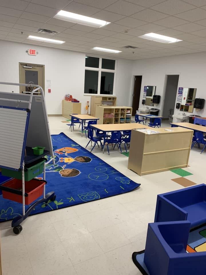 Empty classroom with small tables and chairs, a blue rug, and storage units