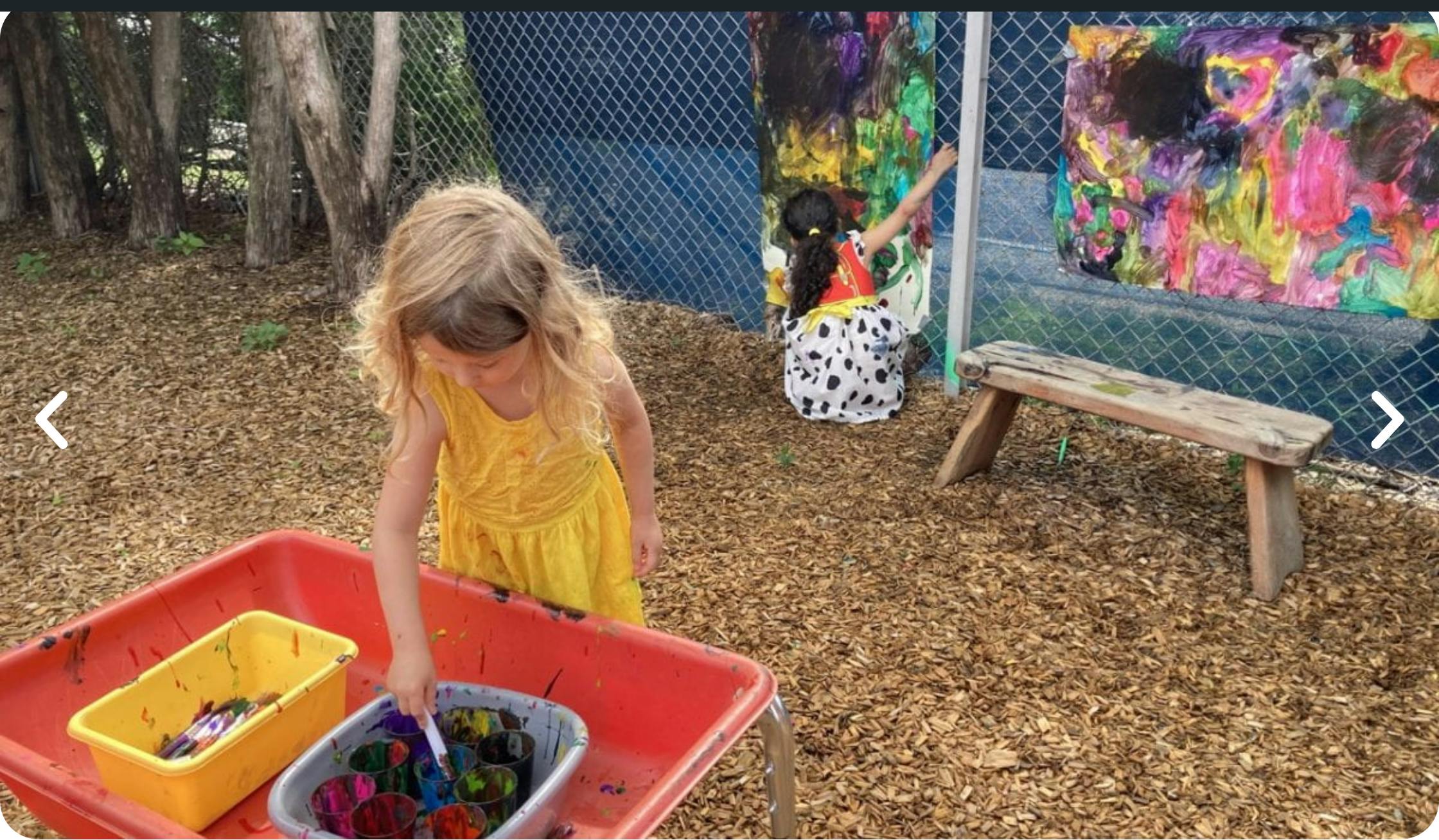 Child in yellow dress painting, another child painting in background