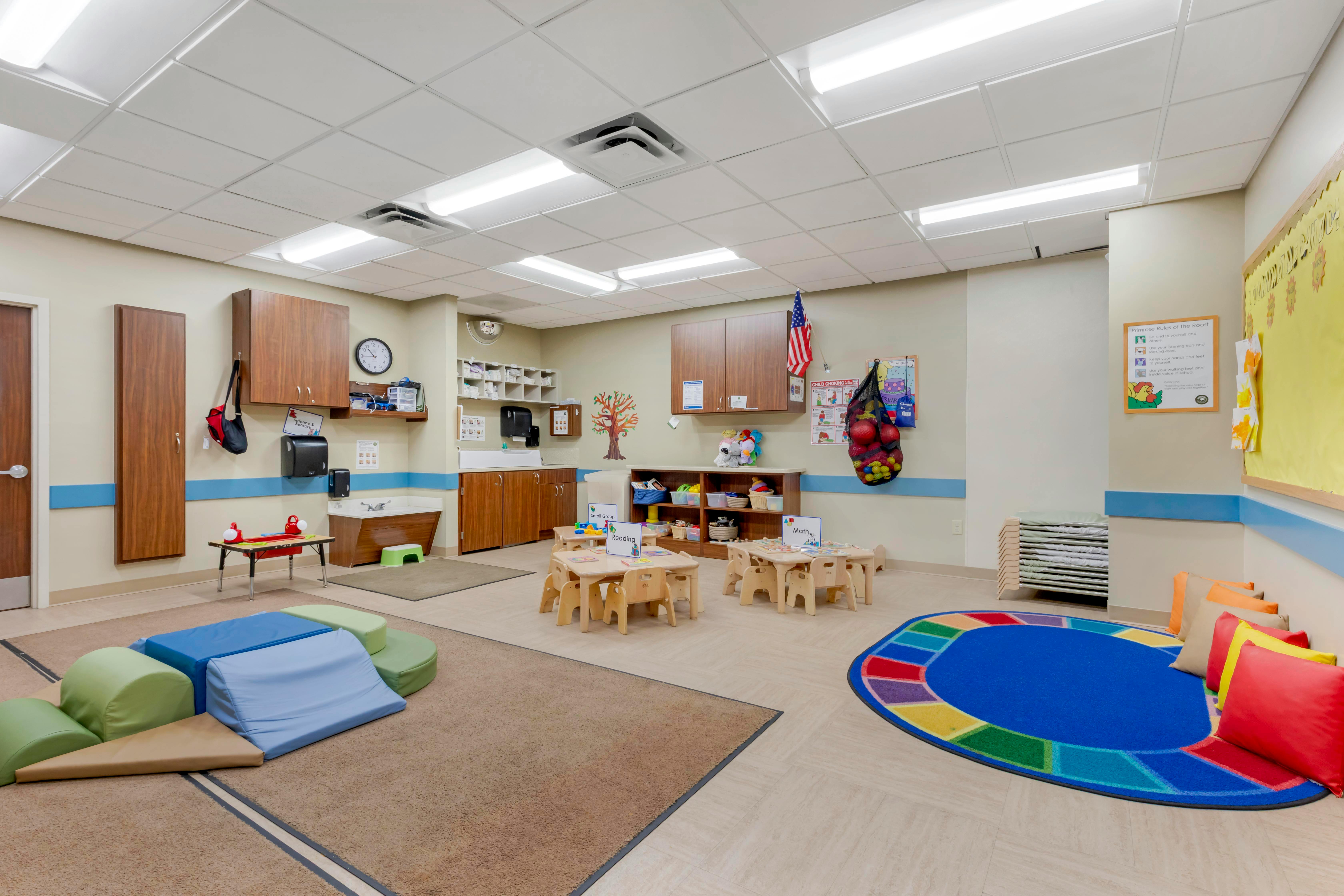 Classroom with child-sized tables and chairs, a soft play area, and activity rugs