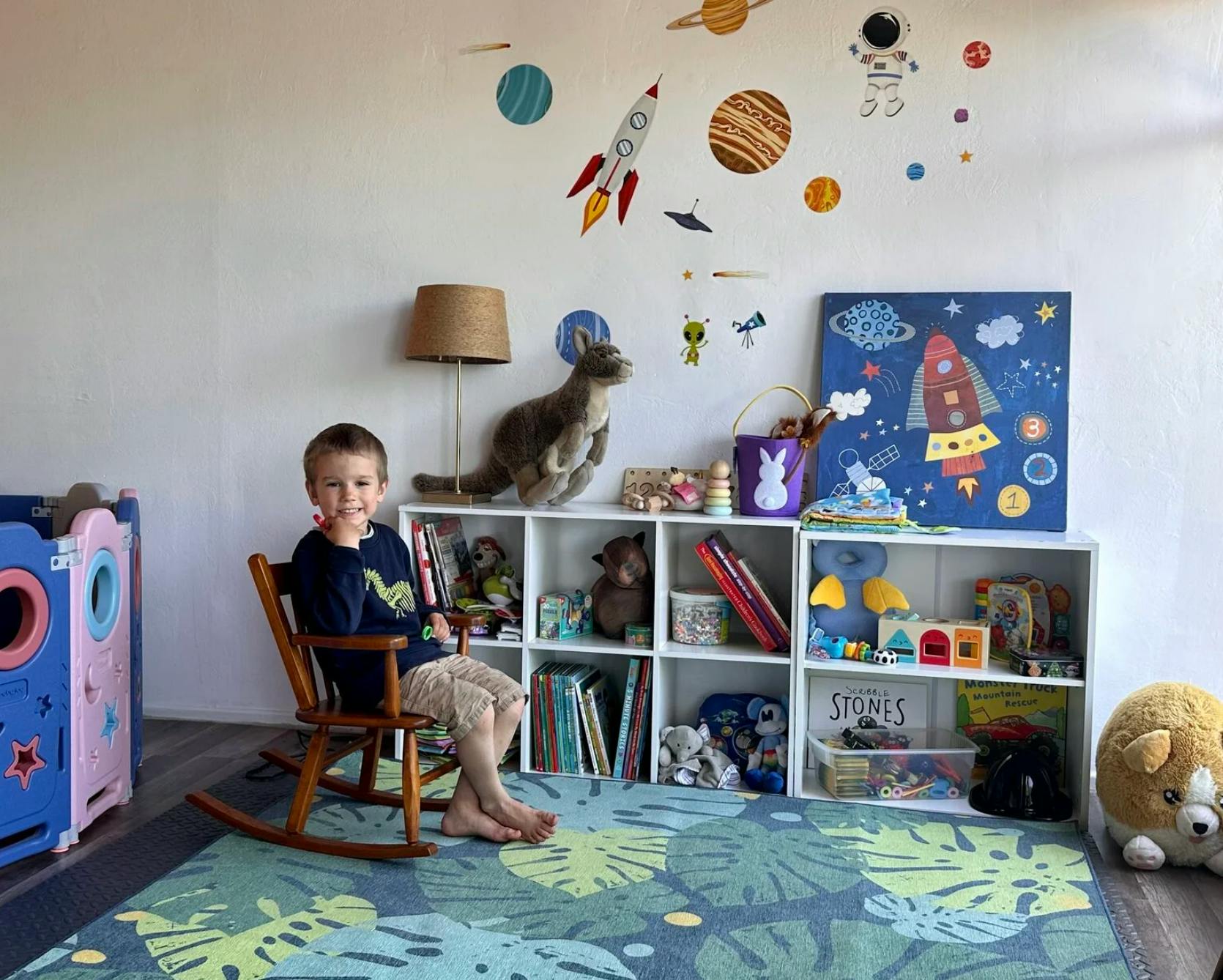 Child sitting in a rocking chair next to a bookshelf with toys