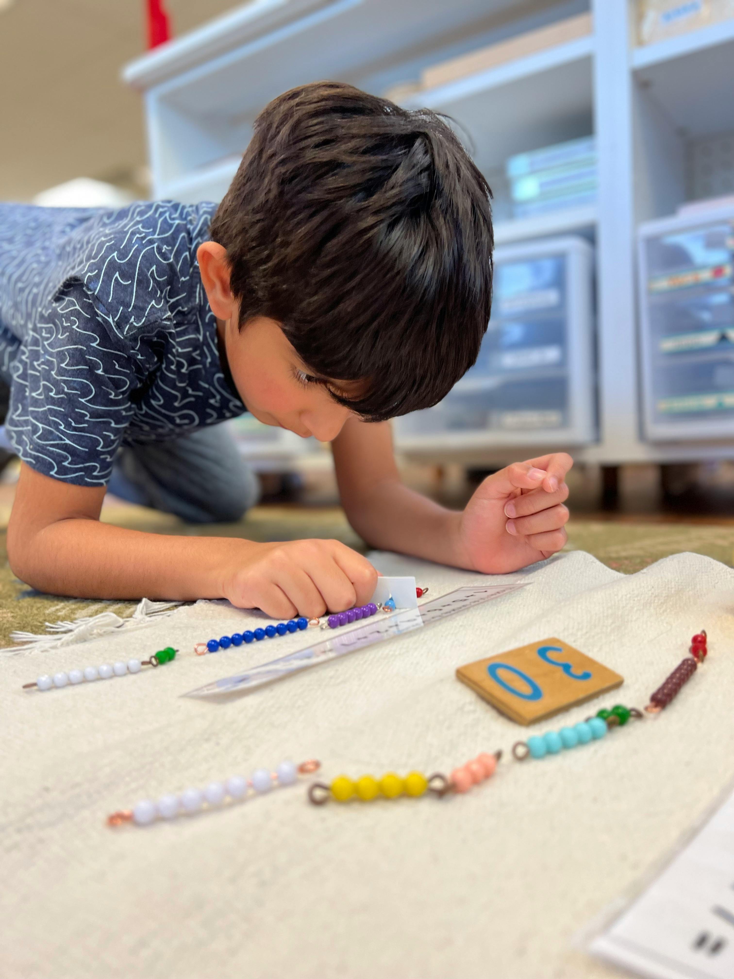 Child on floor looking at colorful beads and a wooden number block