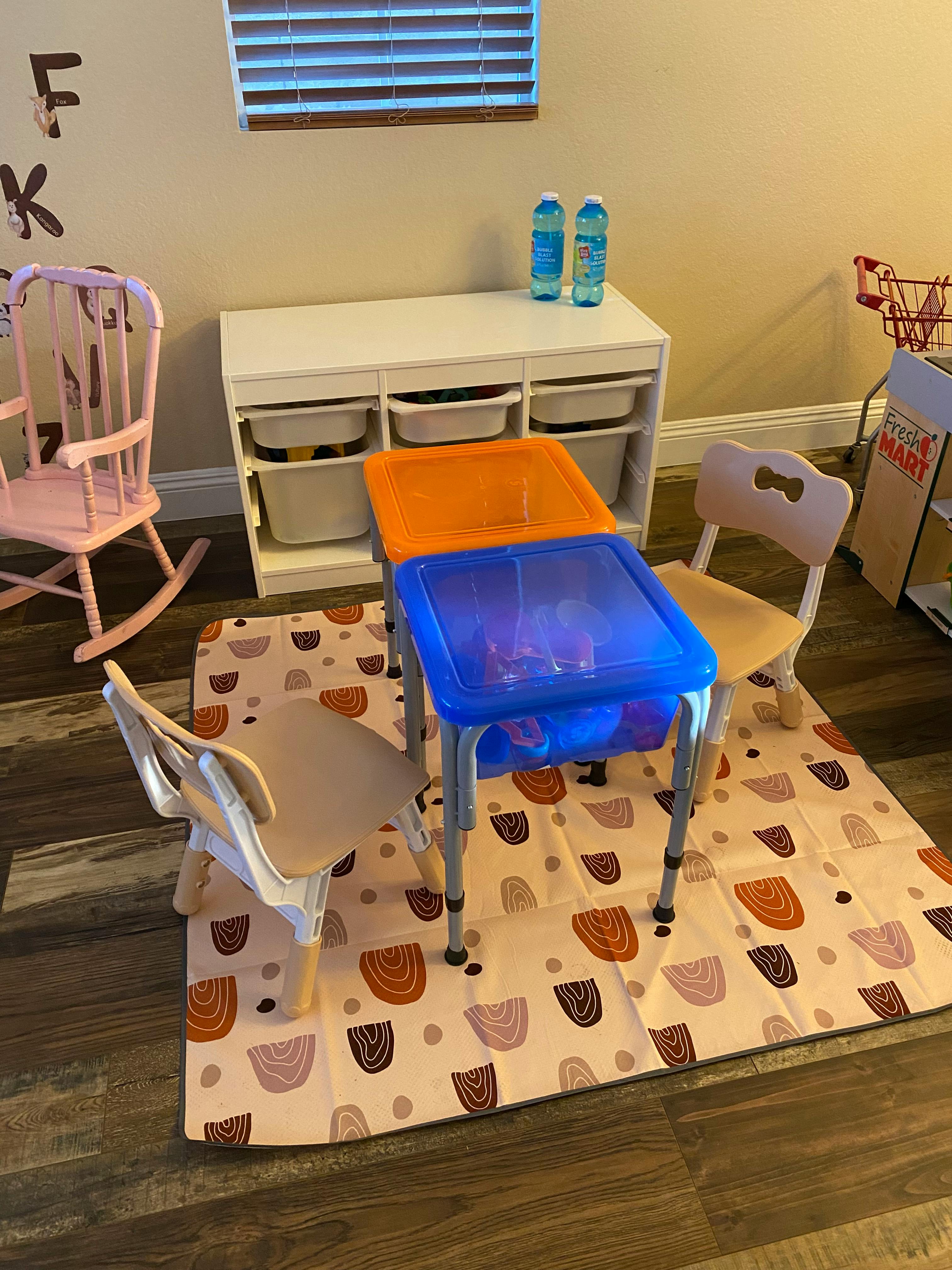 Children's play area with small tables, chairs, and storage bins