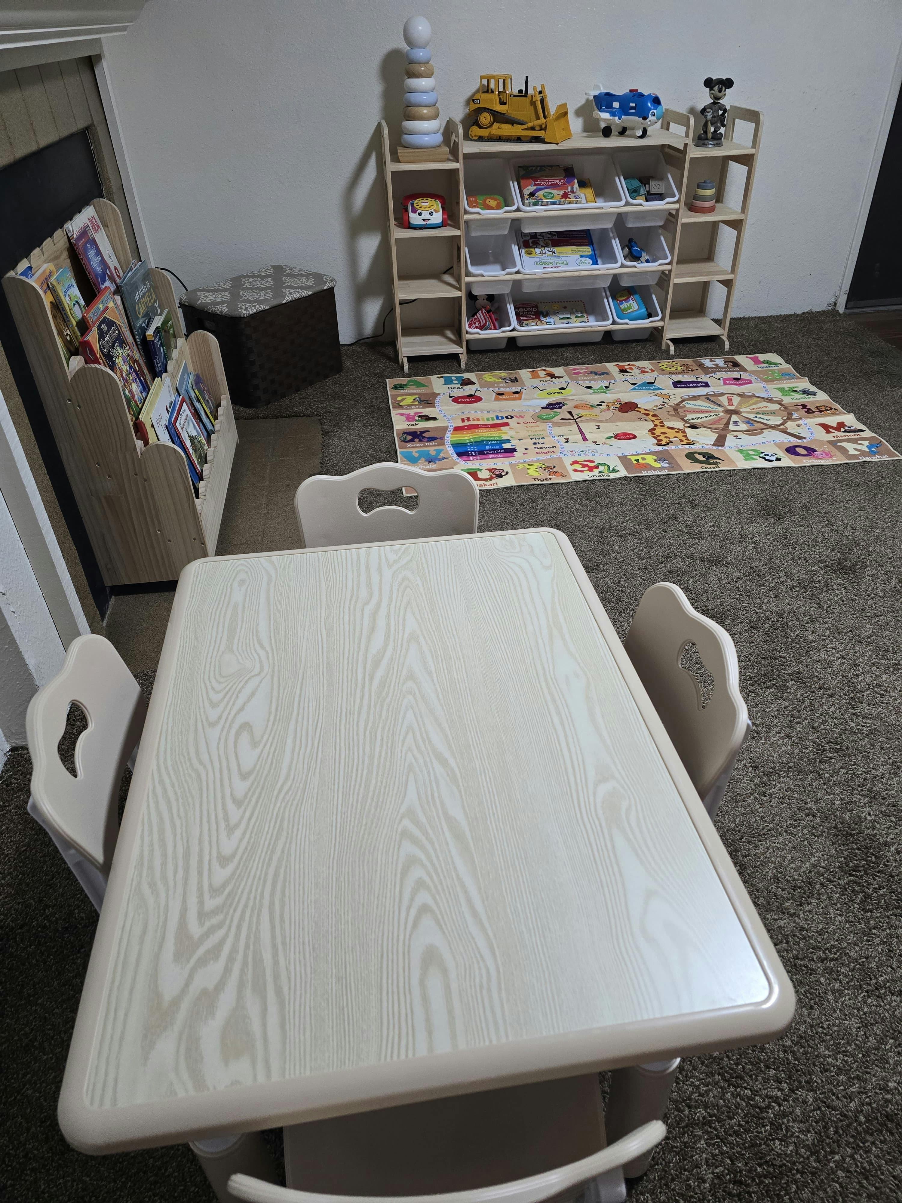 child's play area with a table and chairs, toy shelves, book rack, and play mat