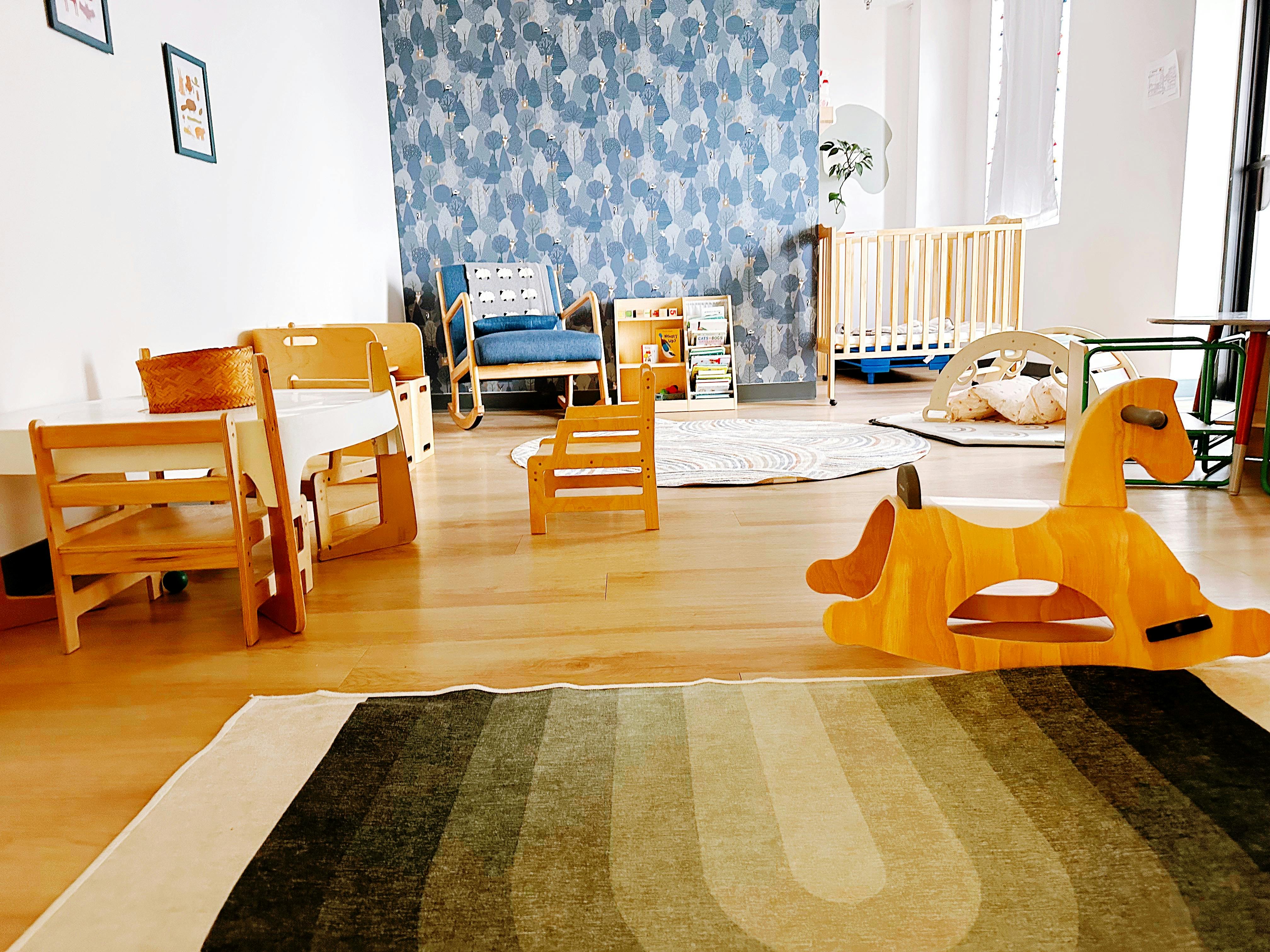 A room with children's furniture, including a rocking horse, crib, and small tables