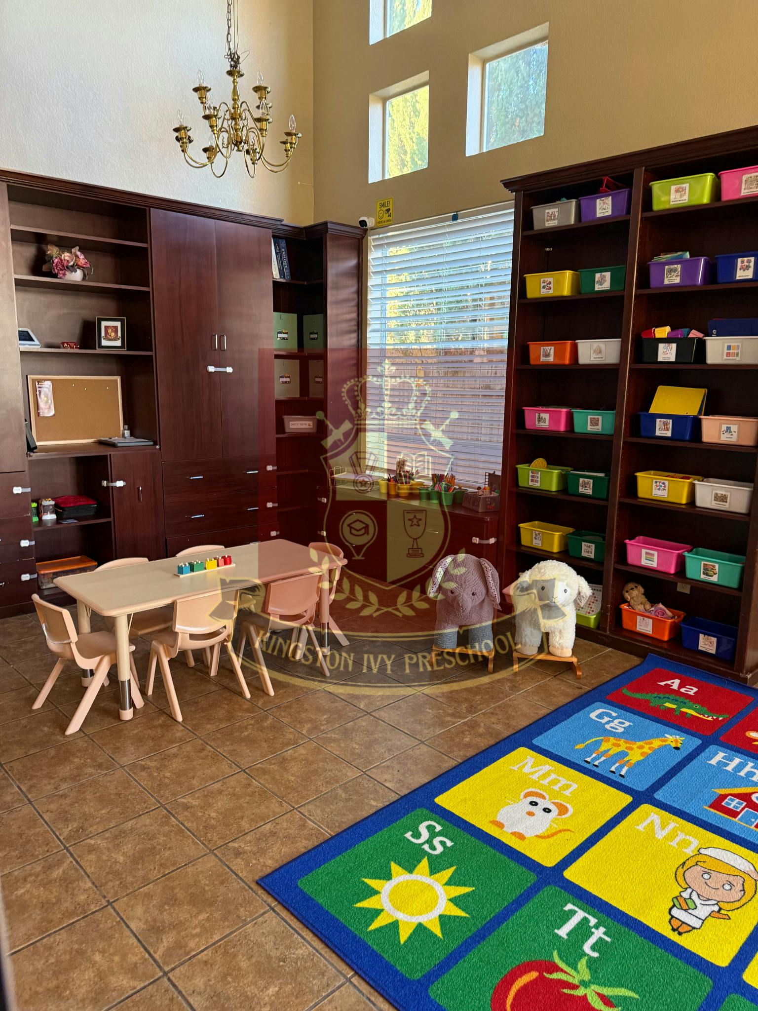Classroom with small tables and chairs, bookshelves, and an alphabet rug