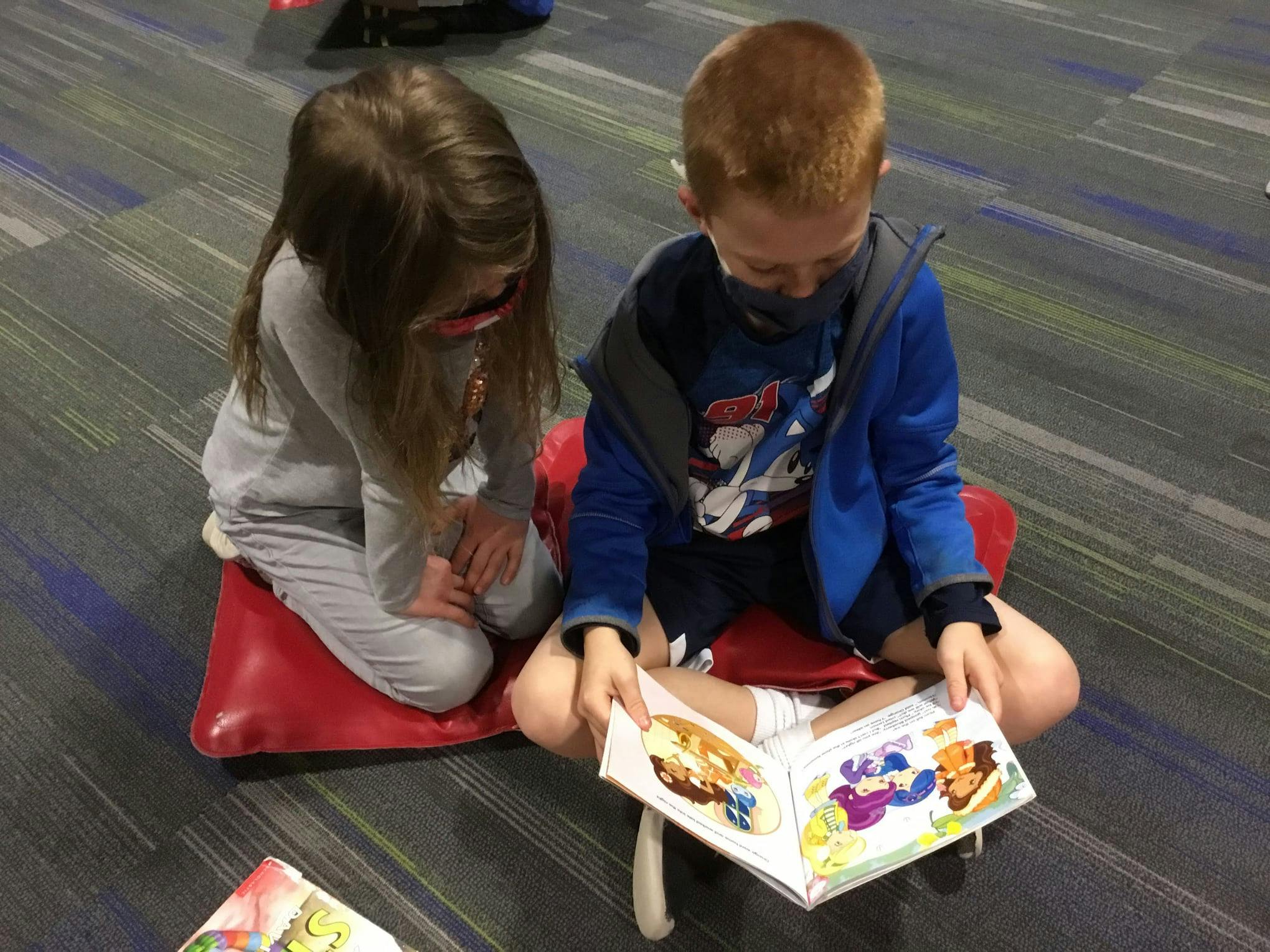 Two children sitting on the floor, one reading a book