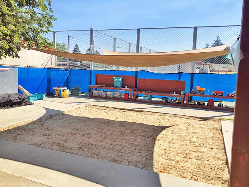 Outdoor play area with a large sandbox and a shade sail