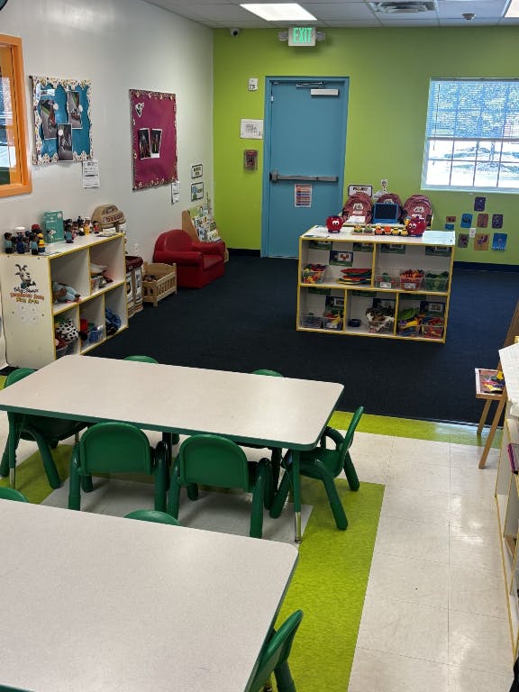 Classroom with small tables and chairs, shelves with toys, and a blue door