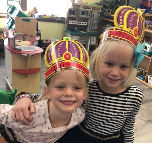 Two children wearing crowns in a classroom