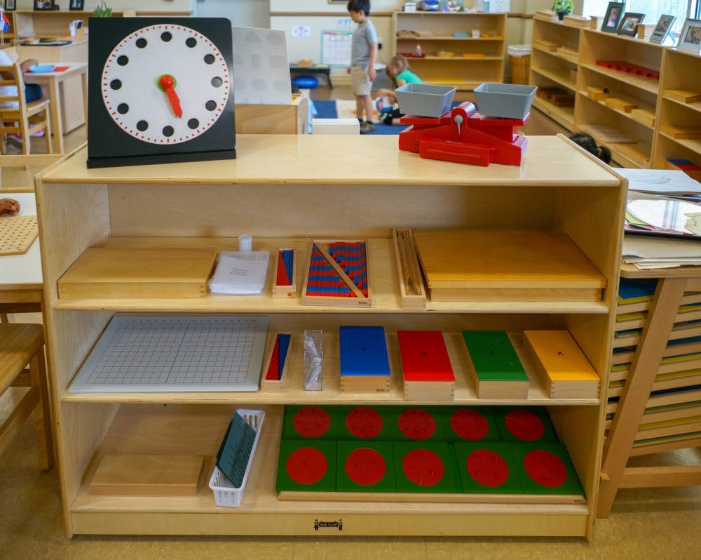 Shelf with a clock, scale, and various learning materials in a classroom
