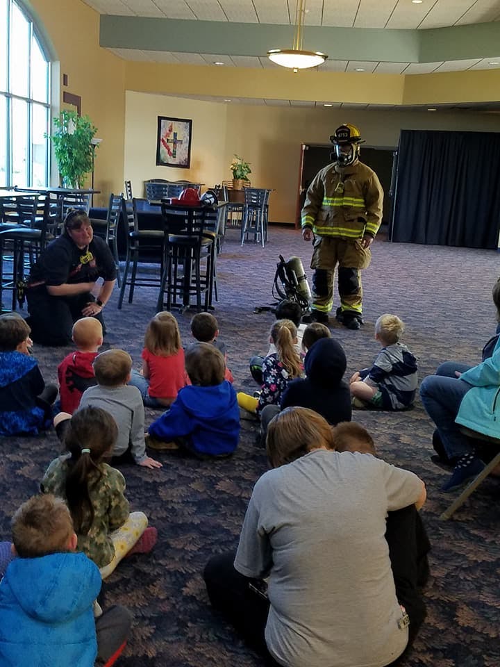 Firefighter in full gear standing in front of children sitting on the floor