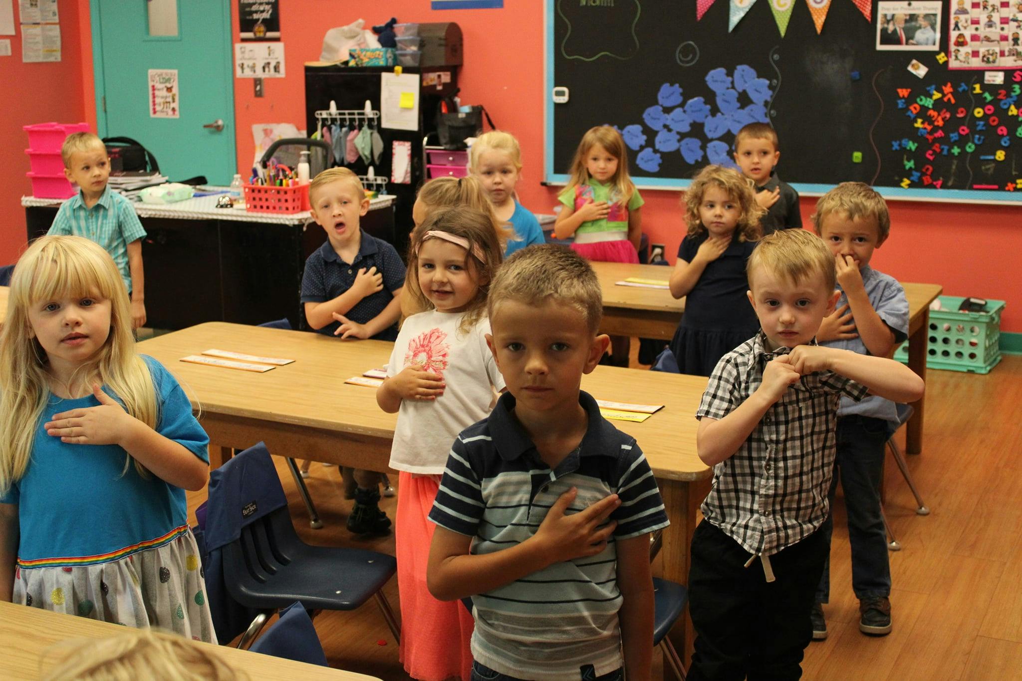 Children standing with hands over hearts in a classroom