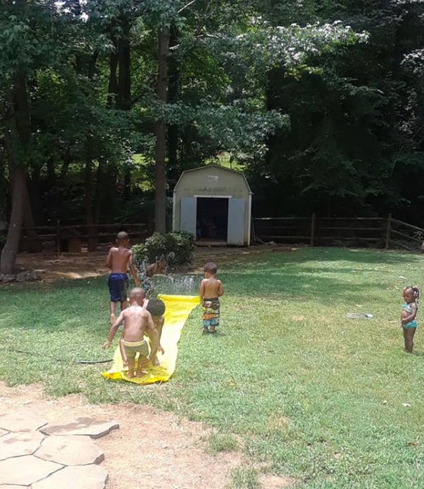 Children playing on a yellow slip and slide in a grassy yard