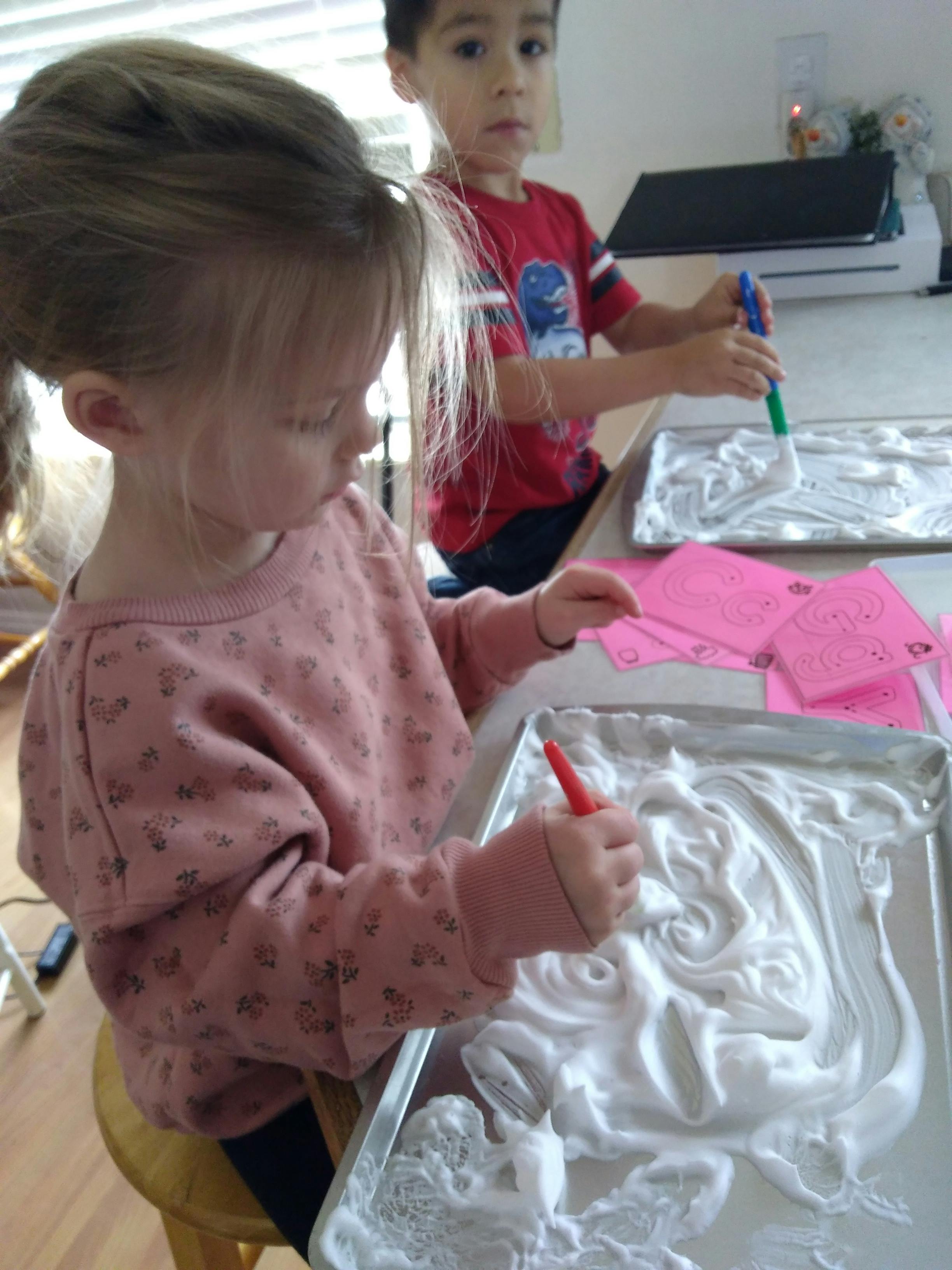 Two children drawing in shaving cream on baking sheets