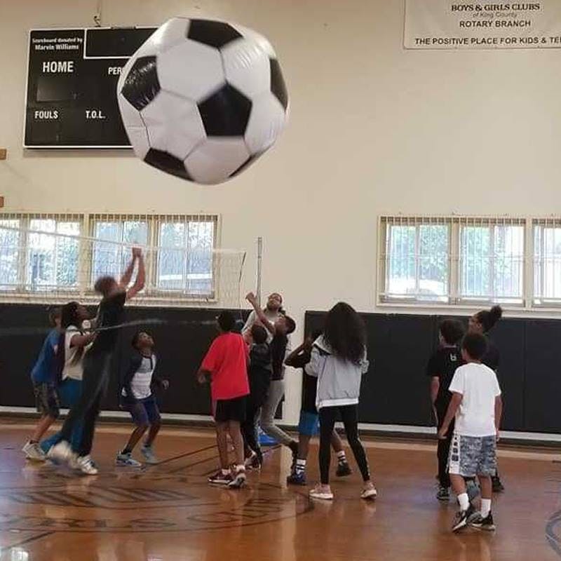 Children playing with a large inflatable soccer ball in a gym
