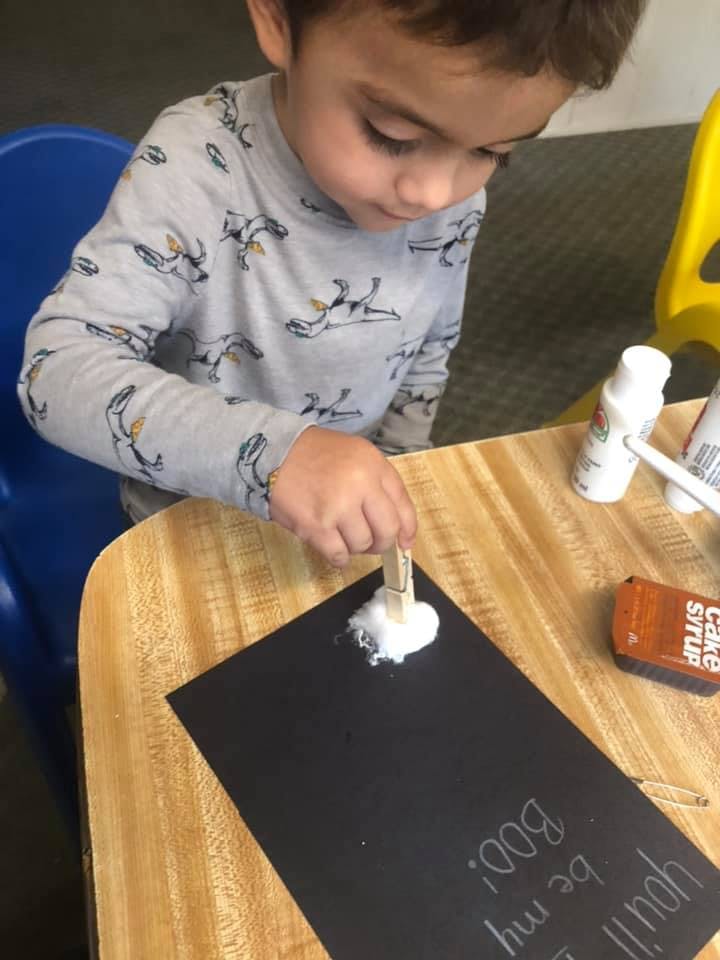 Child using a clothespin to dab white paint onto black paper