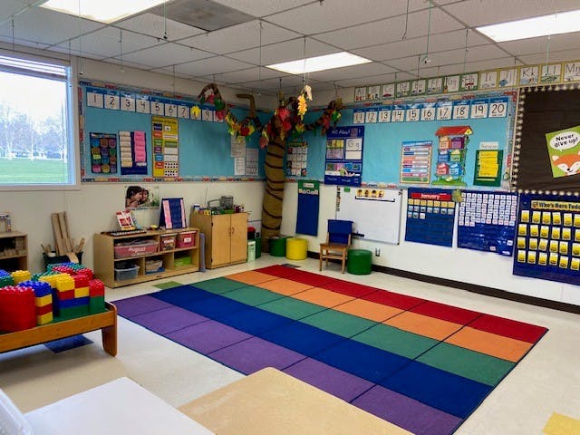 Classroom with a rainbow rug, bulletin boards, and a tree decoration