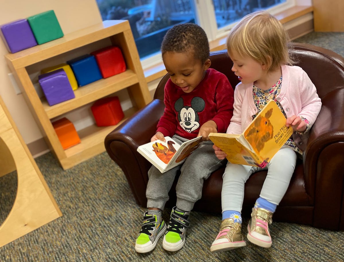 Two children sitting on a chair reading books