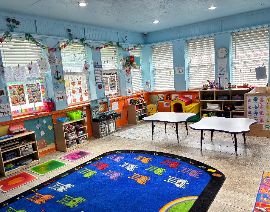 Classroom interior with small tables and a colorful alphabet rug