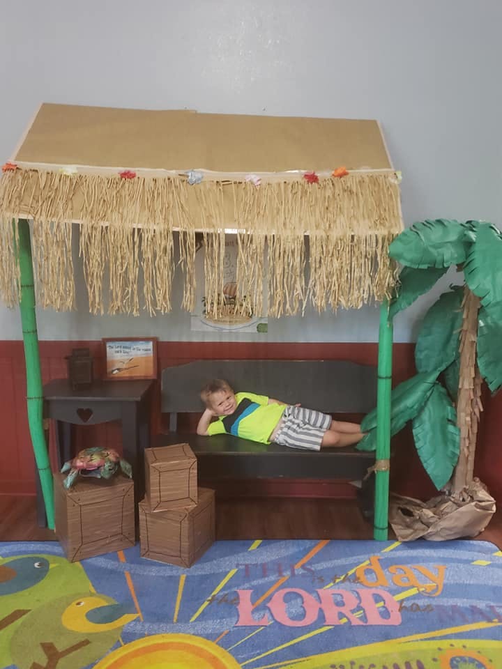 Child lying on a bench under a straw-fringed canopy