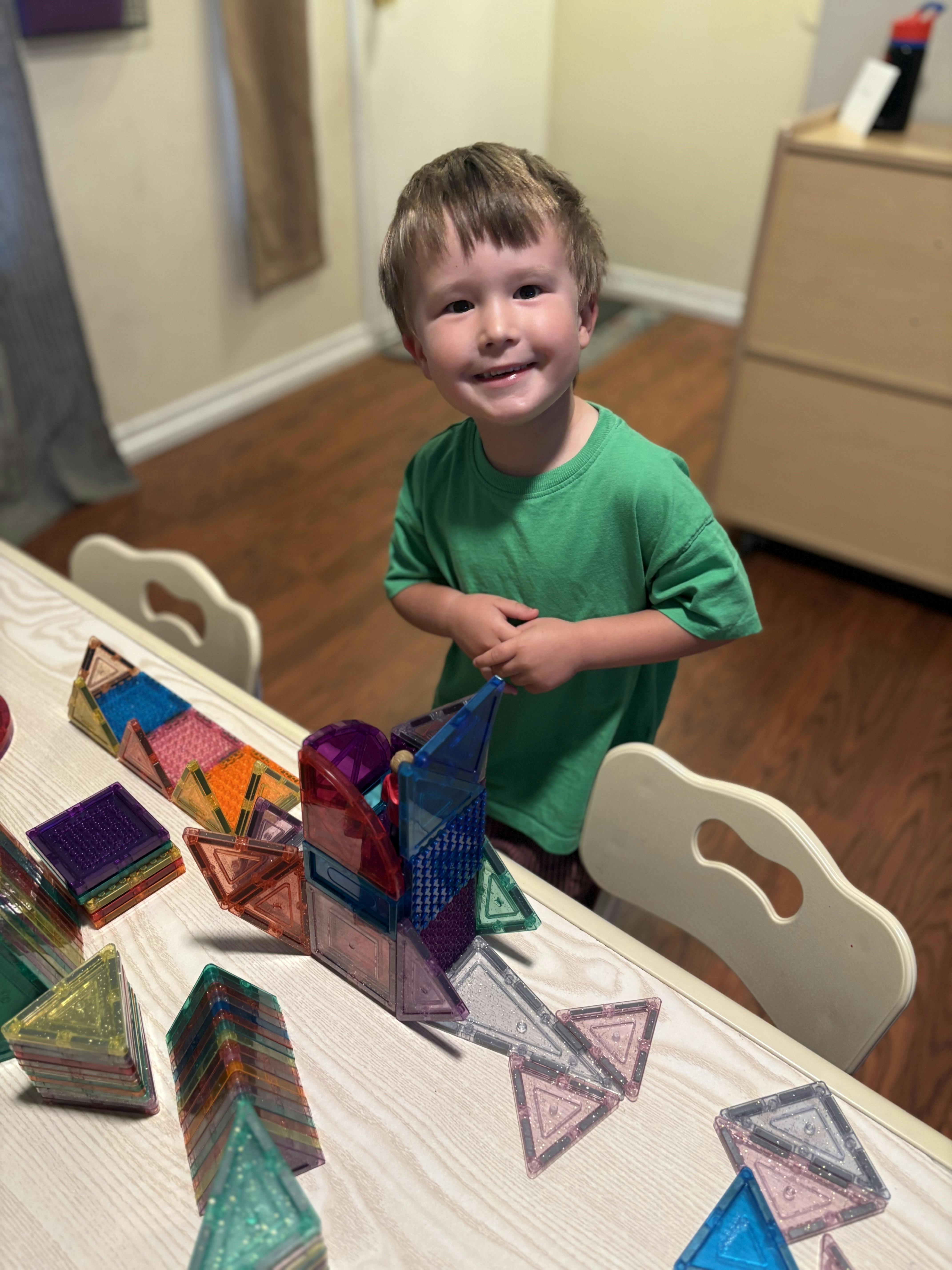 Child standing at a table with magnetic building tiles