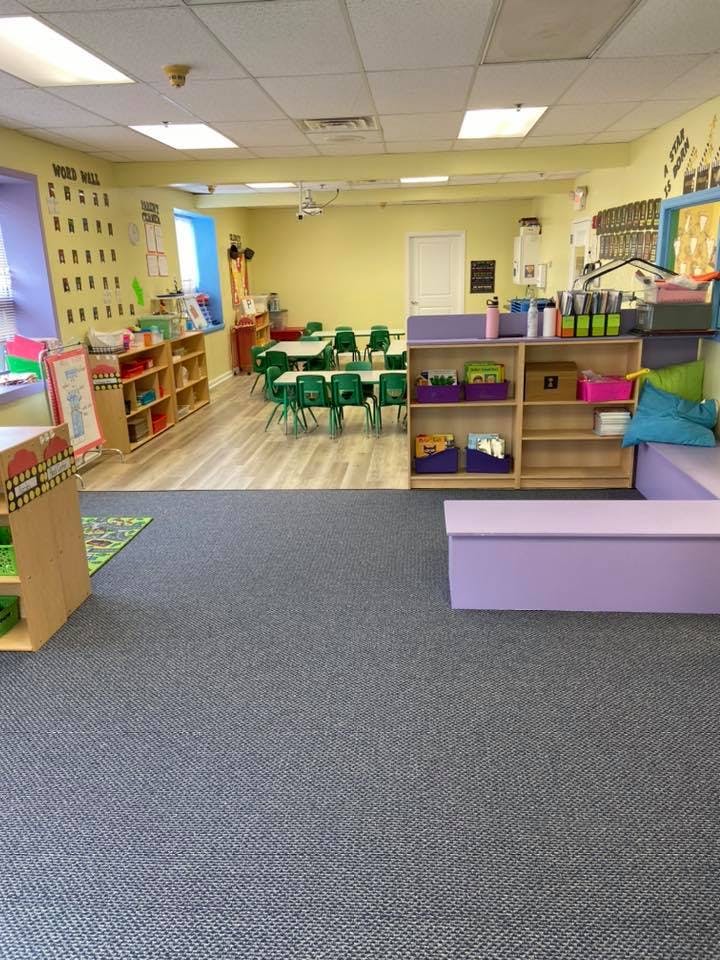 Classroom with small tables and chairs, shelves with supplies, and purple seating