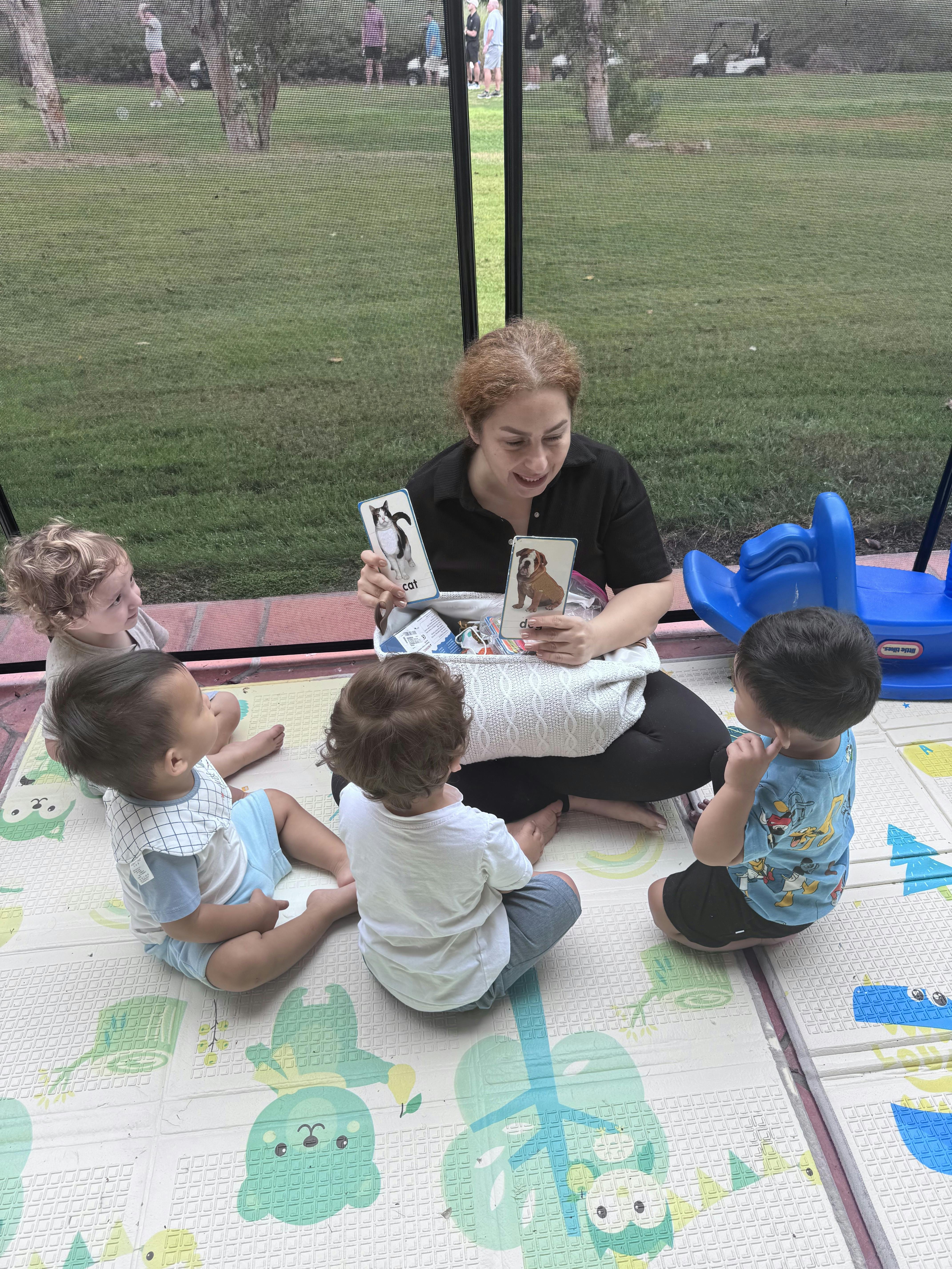 Adult showing flashcards to children sitting on a play mat