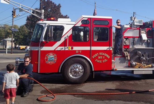 Person kneeling next to a child with a fire truck in the background