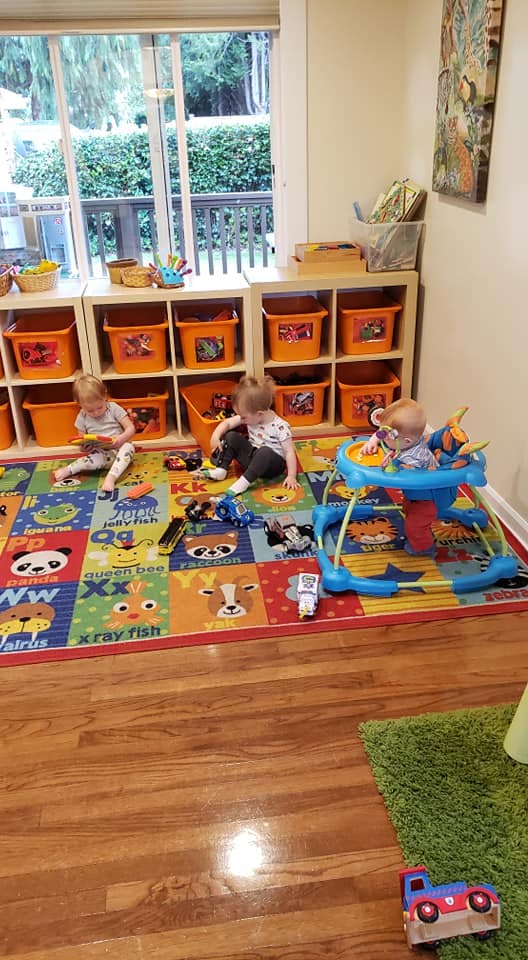Three children playing on a colorful rug in a room with shelves