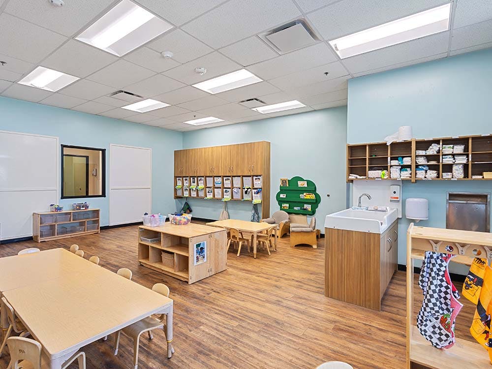 Classroom with tables, chairs, storage cubbies, and a changing station with sink