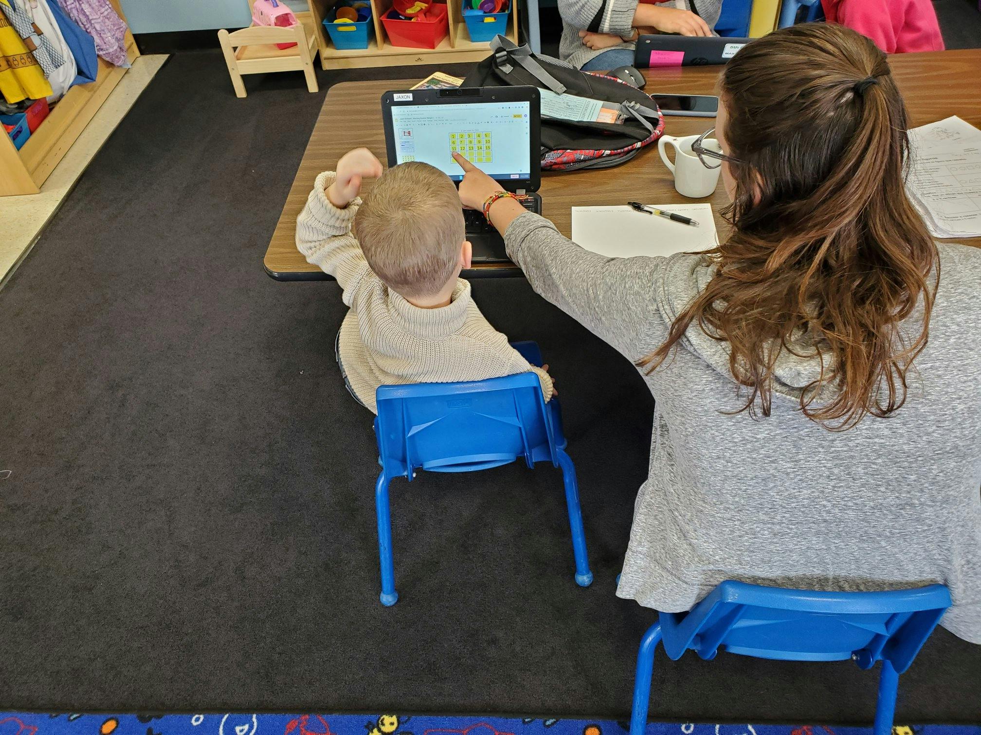 Person pointing at a laptop screen with a child sitting next to them