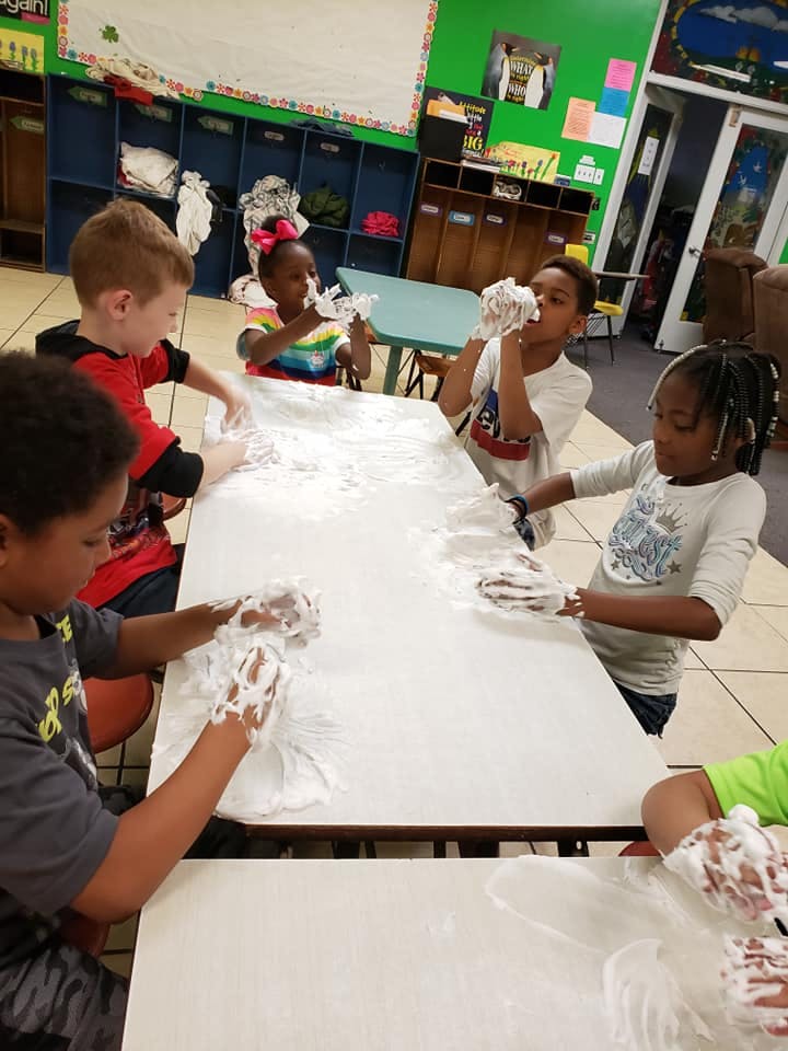 Children playing with shaving cream on a table in a classroom