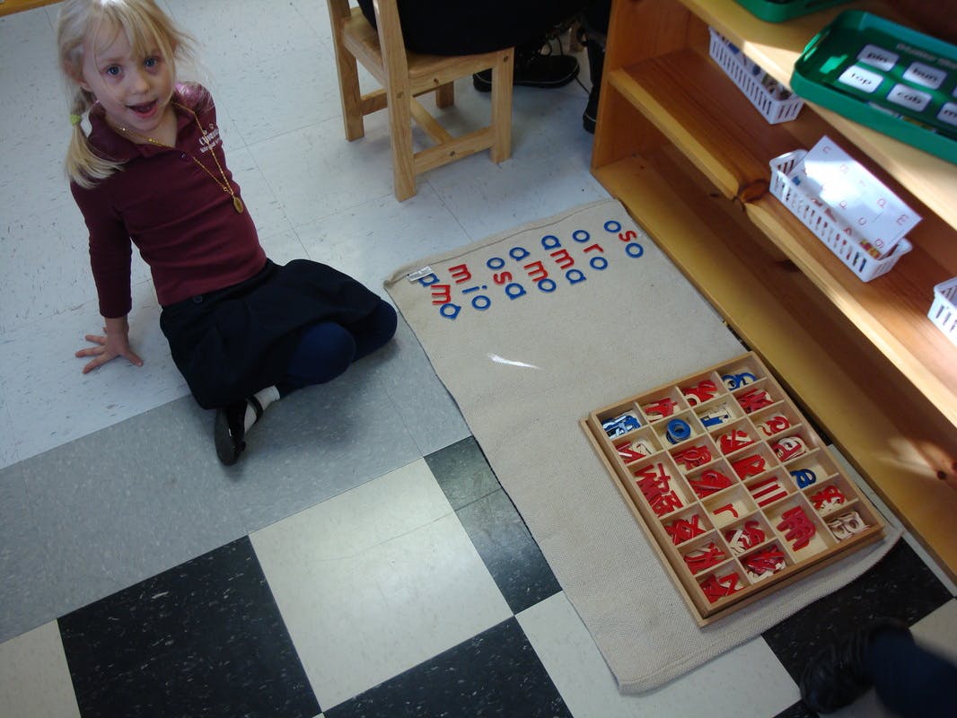 Child sitting on floor next to a mat with letter tiles