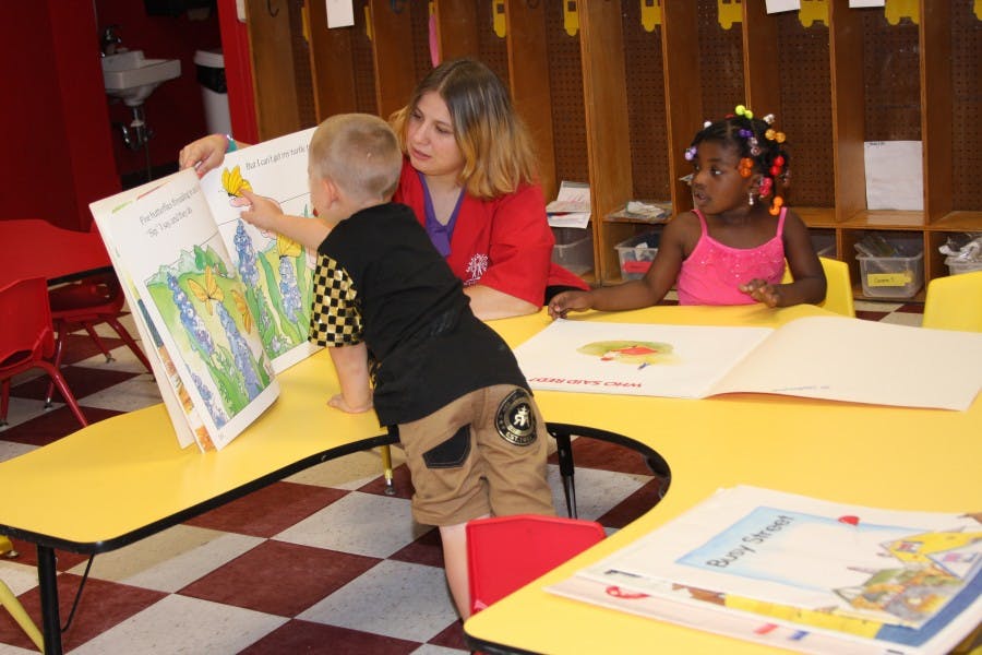 Person and two children looking at books in a classroom