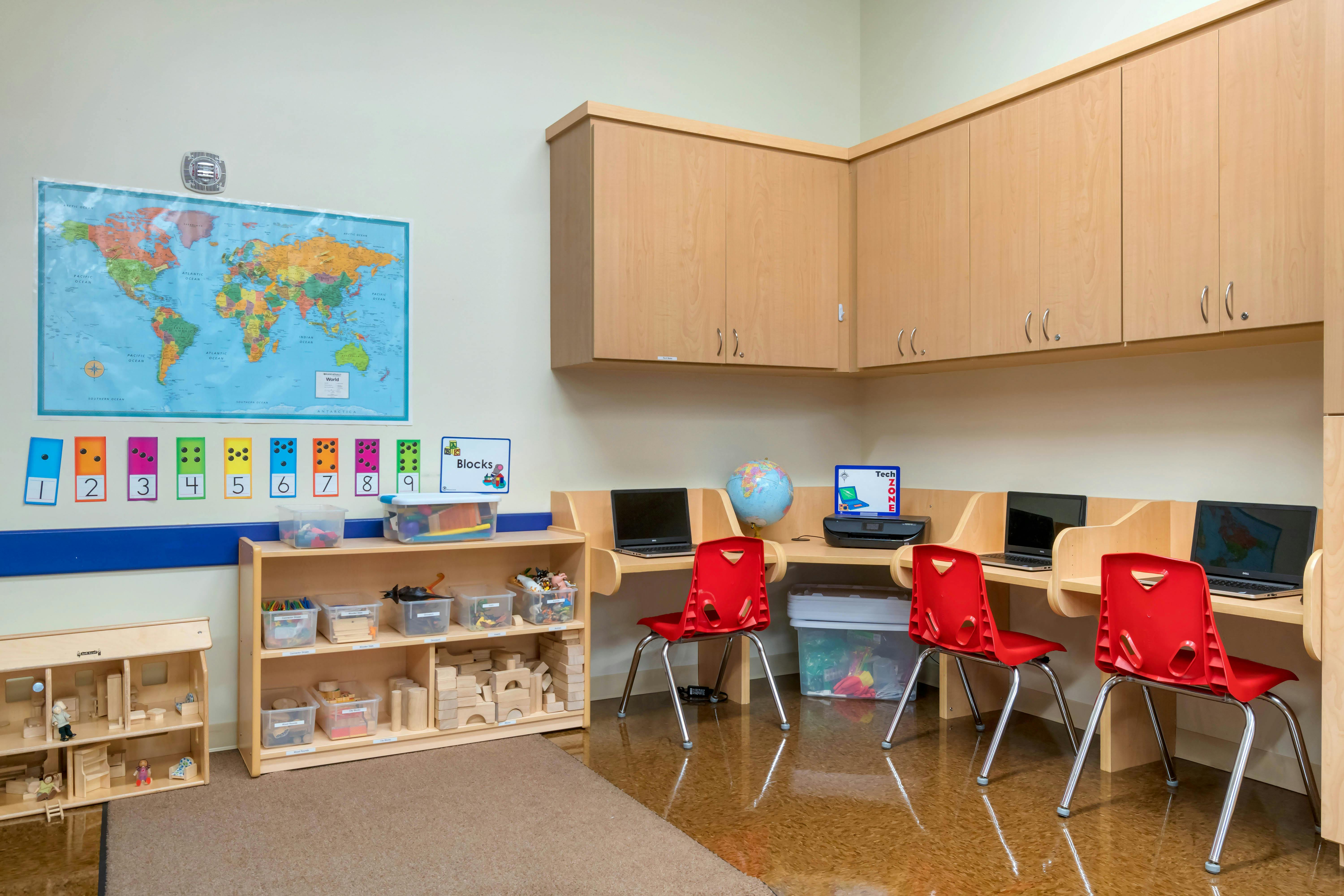 Classroom with world map, number cards, wooden block shelves, and computer stations
