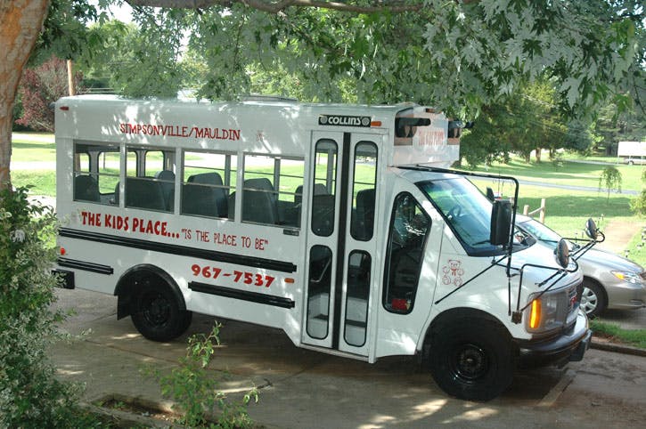 White shuttle bus with "THE KIDS PLACE" written on its side